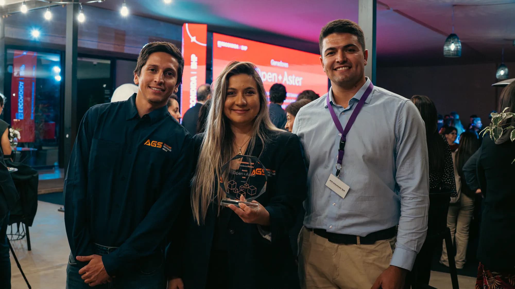 Tres integrantes de AGS en el evento, sosteniendo el galvano de Open Aster grabado con el logo de la empresa